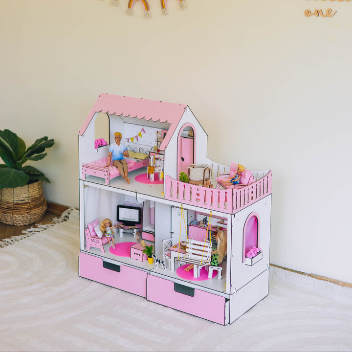 Pink dollhouse with furniture and accessories on a white surface with a decorative wall in the background.
