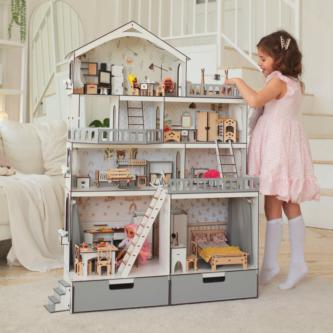 A wooden dollhouse mansion with multiple floors and a young girl playing with it. The dollhouse is white and gray, and it appears to be made of wood with detailed furniture sets inside.