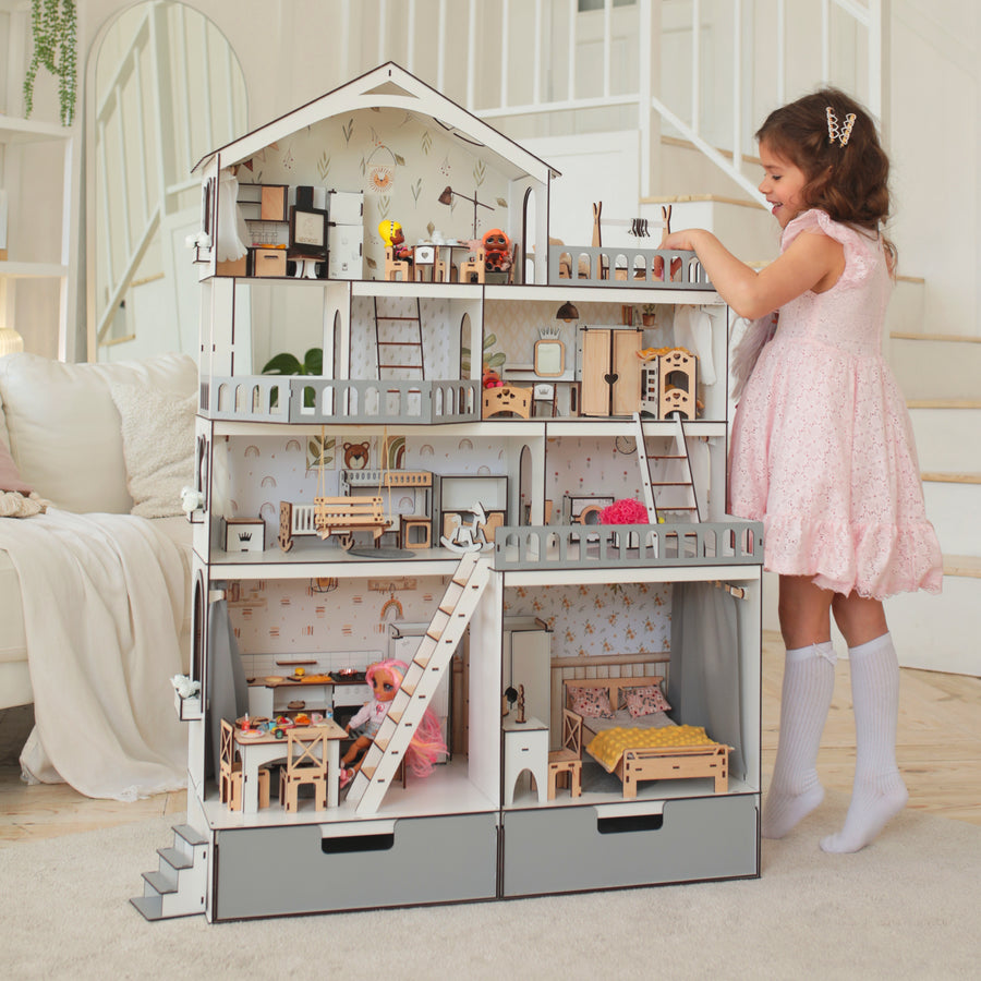 A wooden dollhouse mansion with multiple floors and a young girl playing with it. The dollhouse is white and gray, and it appears to be made of wood with detailed furniture sets inside.
