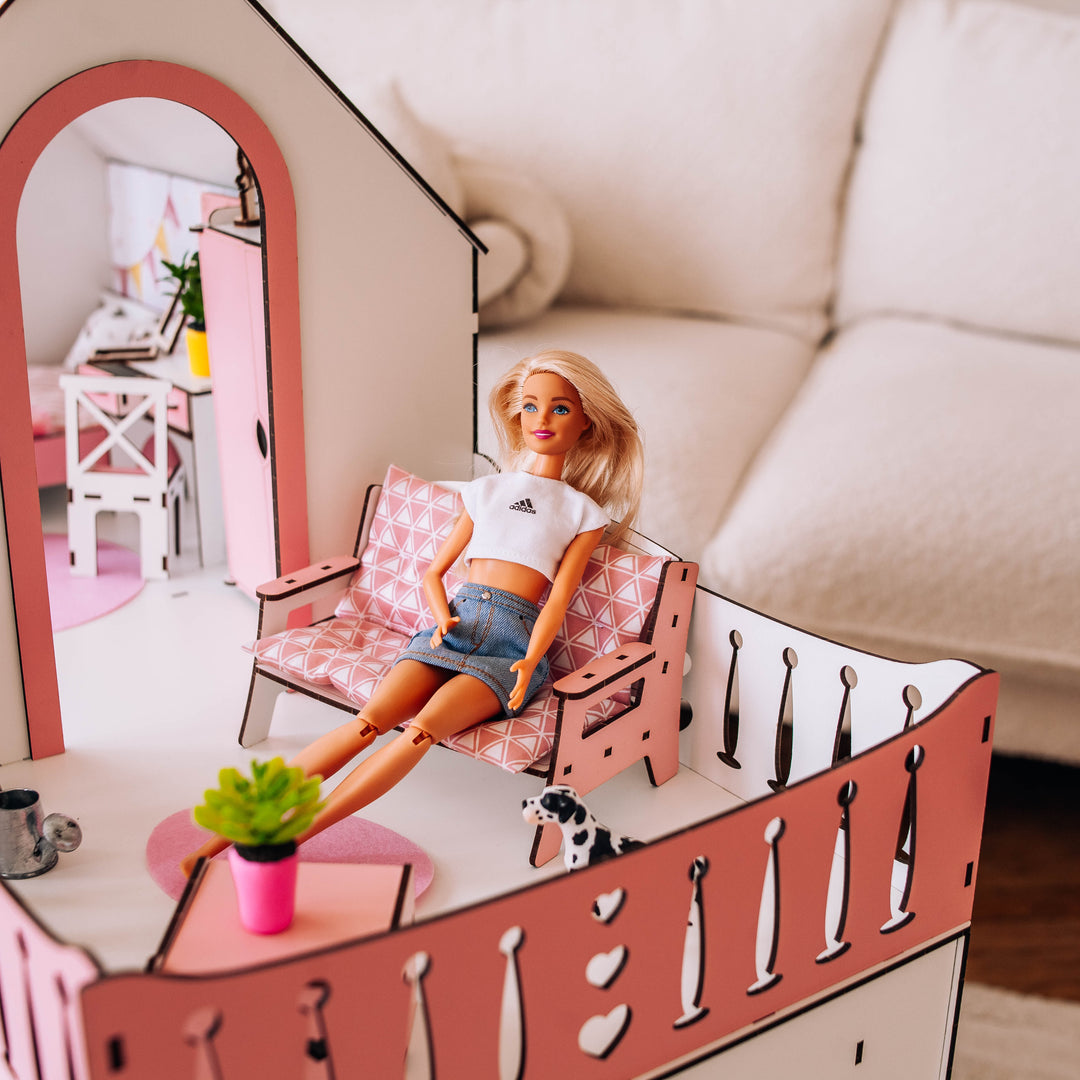 Barbie doll sitting on a pink dollhouse with a white sofa in the background