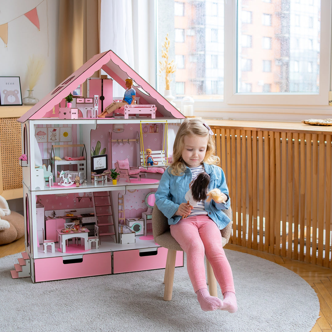 Child playing with a pink dollhouse in a bright room.