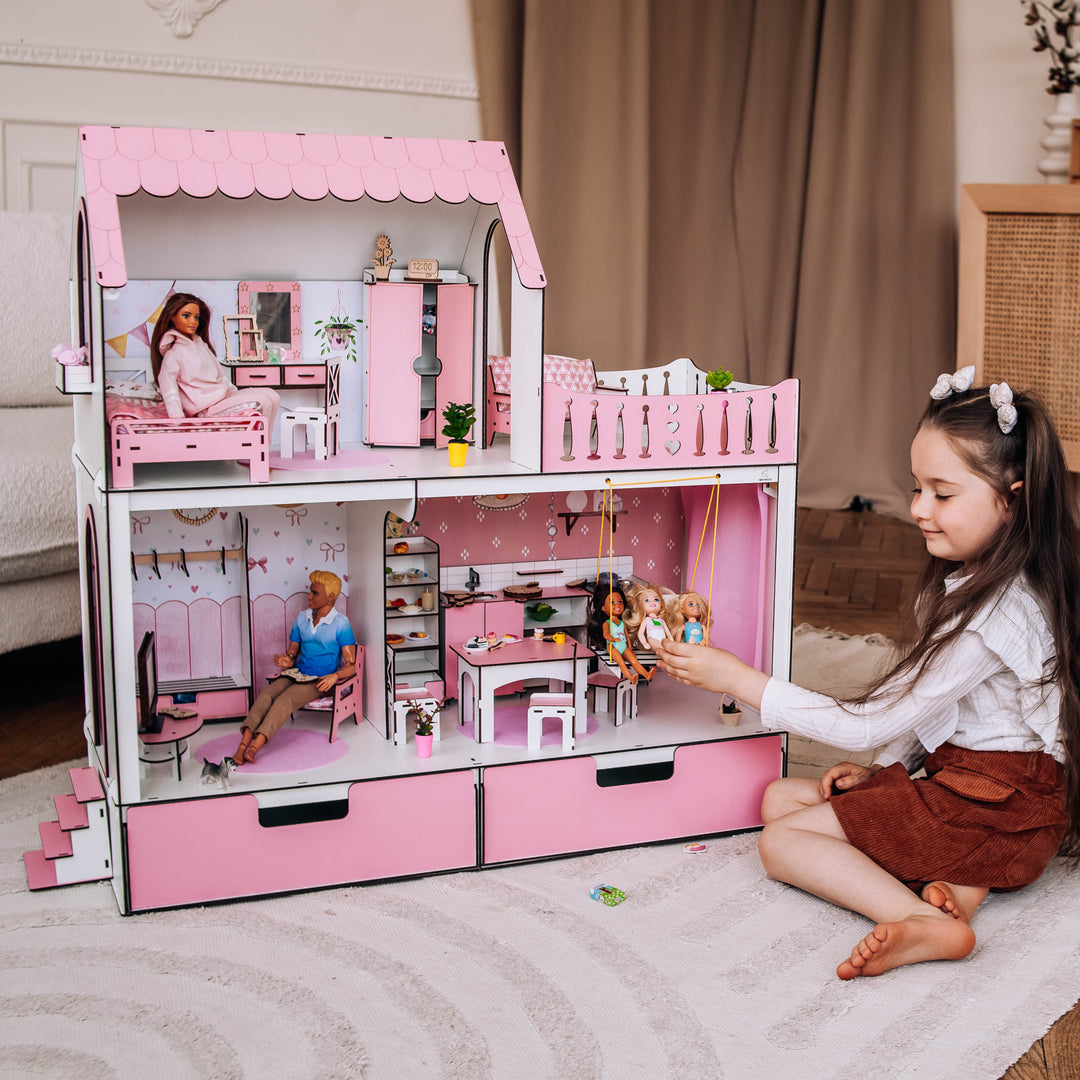 Child playing with a pink dollhouse in a room with wooden flooring and a cabinet.