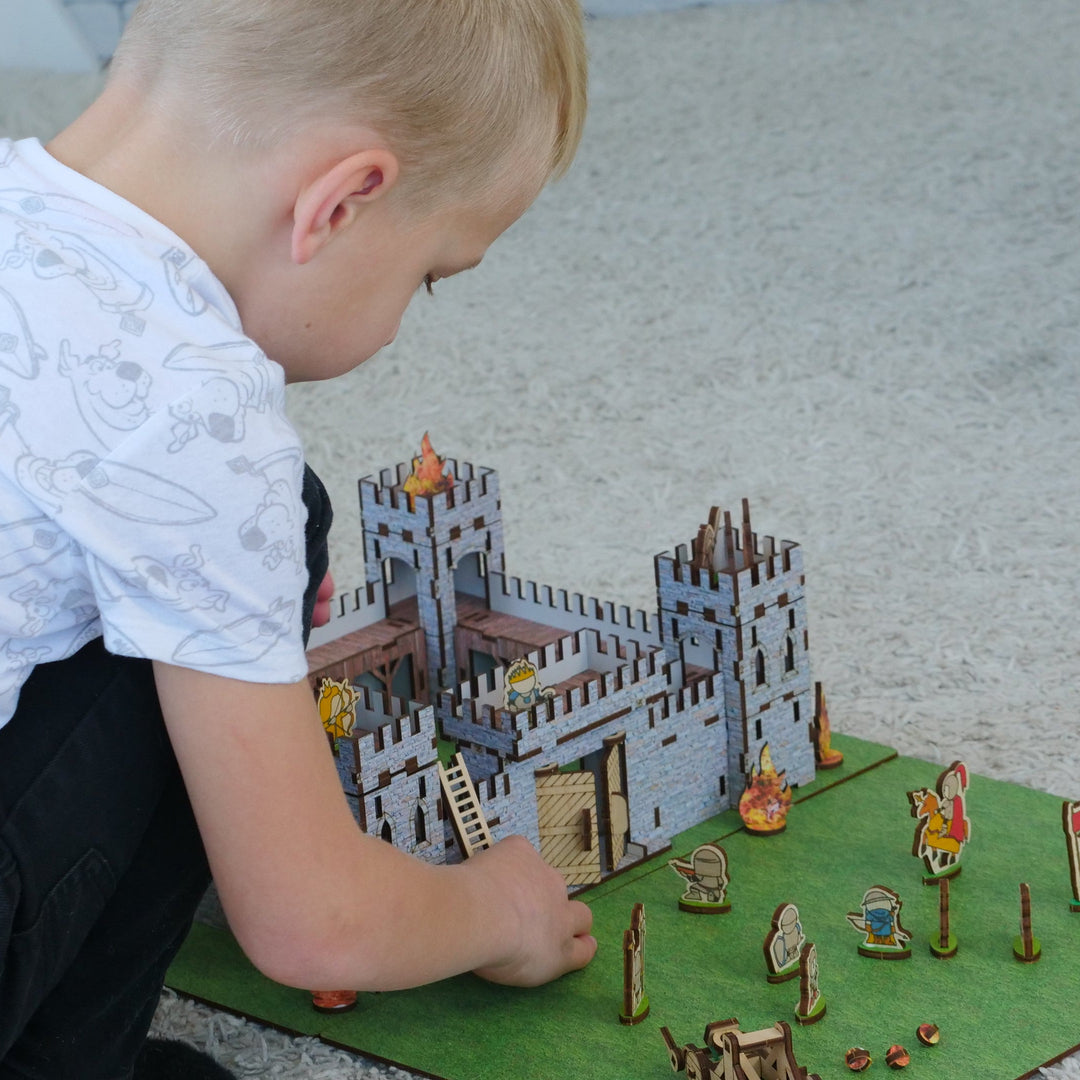 Child playing with a toy castle and figures on a green mat.