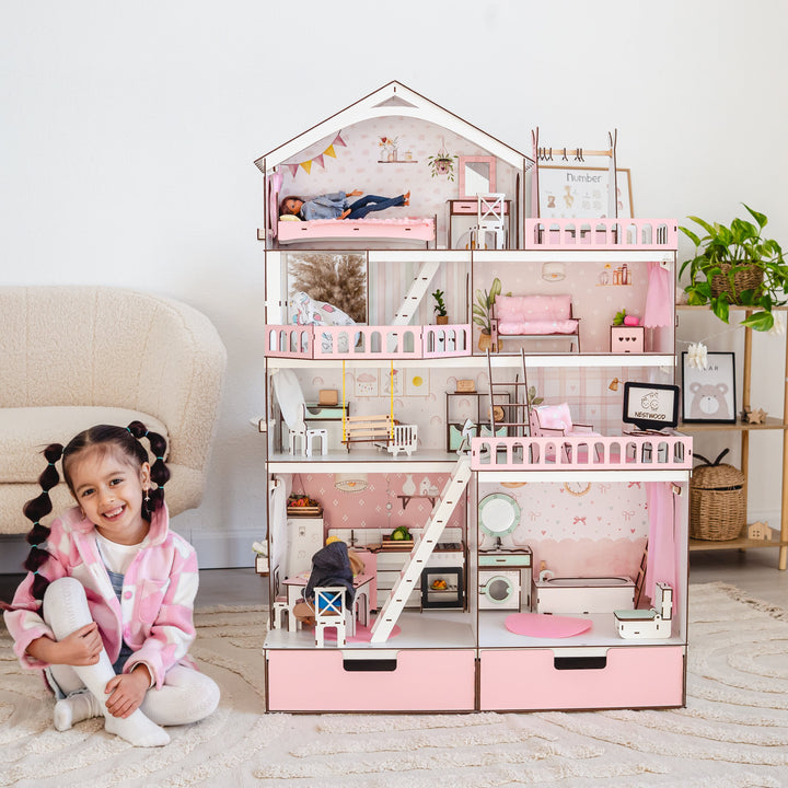 Child sitting next to a pink dollhouse in a room with a couch and plant.