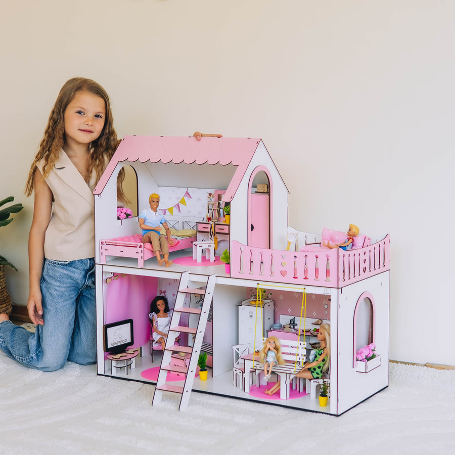Young girl standing next to a pink dollhouse with furniture and dolls inside.