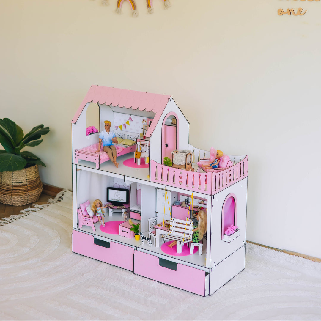 Pink dollhouse with furniture and accessories on a white surface with a decorative wall in the background.