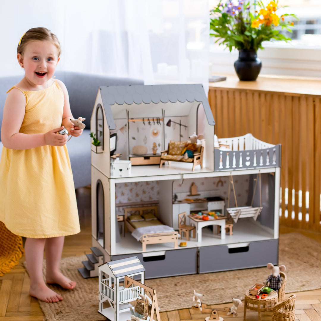 Young girl playing with a toy dollhouse in a bright room with large windows.