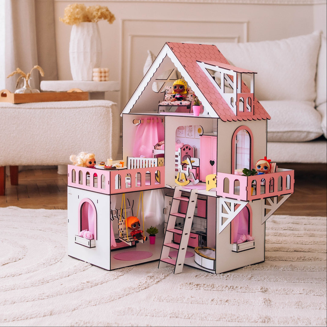 A pink and white wooden dollhouse with a red roof, miniature ladder, and tiny furniture pieces, displayed on a light-colored rug in a bright, modern living room.