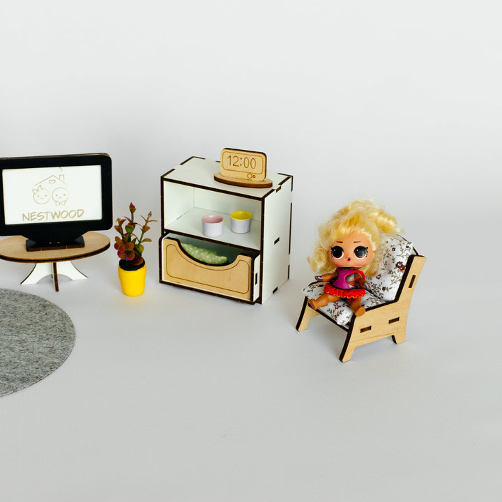 A miniature dollhouse furniture set on a light gray background, featuring a small TV on a round stand, a cabinet with a small plant, and a doll sitting in a chair.