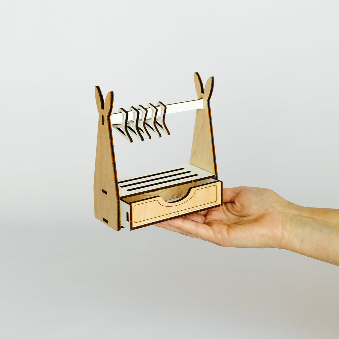 A small wooden hanger rack organizer with a drawer and hanging bars, held in a person's hand against a plain light gray background.
