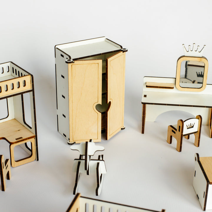 A set of miniature wooden toy furniture pieces, including a crib, cabinet, desk, chairs, and shelving, arranged on a clean white surface against a white background.
