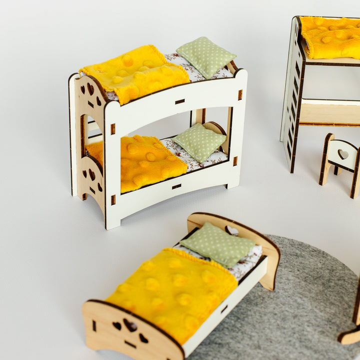 A miniature wooden bunk bed set with yellow bedding and green patterned pillows, shown alongside a matching single bed and small stool on a light gray background.