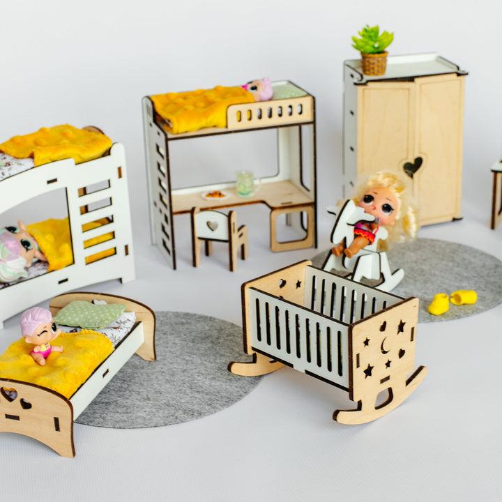 A dollhouse nursery furniture set made of laser-cut light wood, featuring a crib, bunk bed, single bed, dresser, and desk, styled with miniature bedding and a doll on a white background.