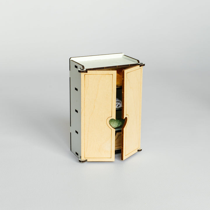 A small wooden cabinet or organizer with two light natural wood doors and a white top surface, shown on a clean light gray studio background.