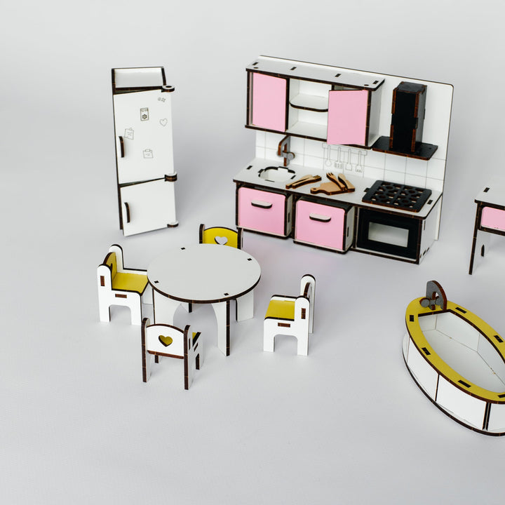 A miniature toy kitchen and dining set displayed on a light gray background. The set includes a small refrigerator, dining table, chairs with yellow seats, a play kitchen with pink cabinets, and a yellow-and-black oval accessory piece.