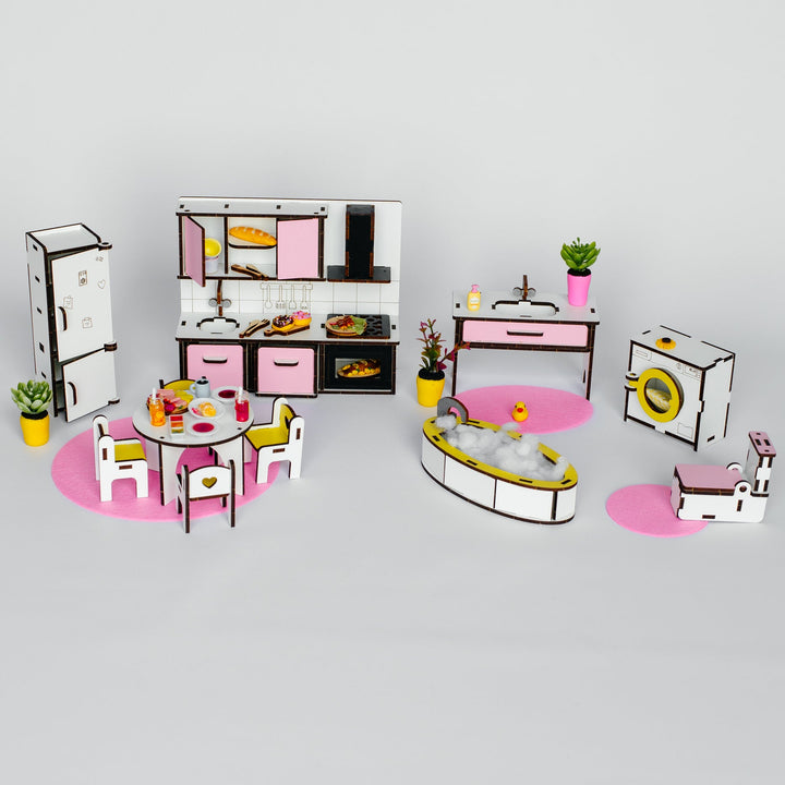 A miniature dollhouse kitchen set with pink and white cabinets, a dining table with pink chairs, a refrigerator, a washing machine, a bathtub, and small potted plants, arranged on a light gray background.