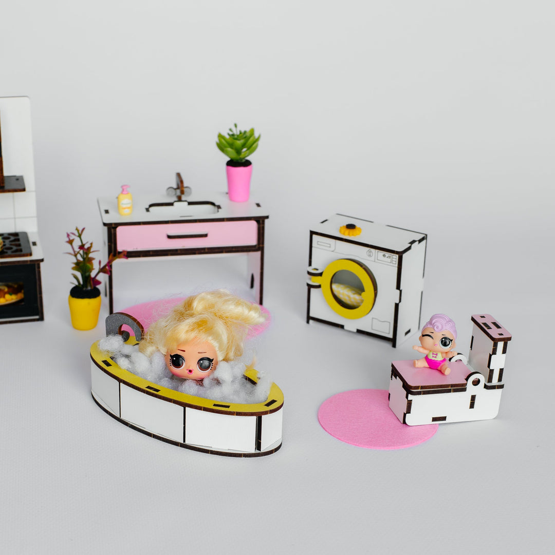 A dollhouse miniature laundry room set featuring a blonde doll in a bathtub, a washing machine, a dryer, a pink sink cabinet, and a small bed with a doll, all arranged on a light gray background.