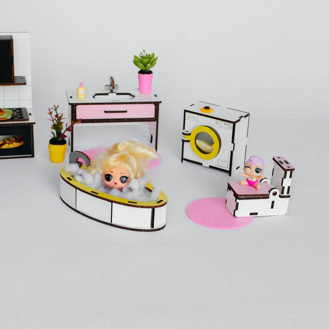 A dollhouse-style bathroom and laundry play set with small figurines, including a bathtub scene, sink table, washing machine, and toilet, arranged on a light gray background.