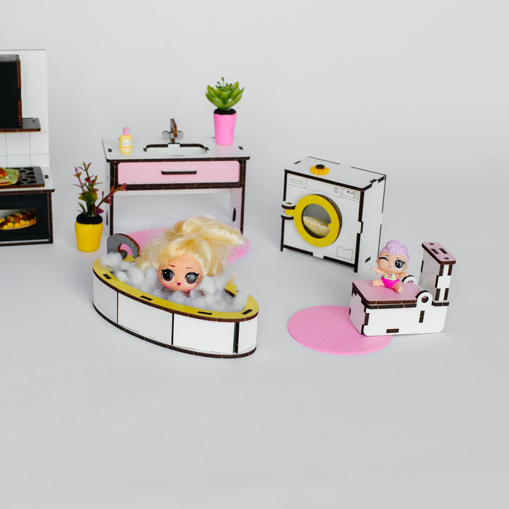 A dollhouse-style bathroom and laundry play set with small figurines, including a bathtub scene, sink table, washing machine, and toilet, arranged on a light gray background.