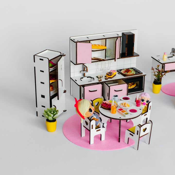 A miniature dollhouse kitchen set with a refrigerator, dining table, chairs, and small potted plants, displayed on a light gray background.
