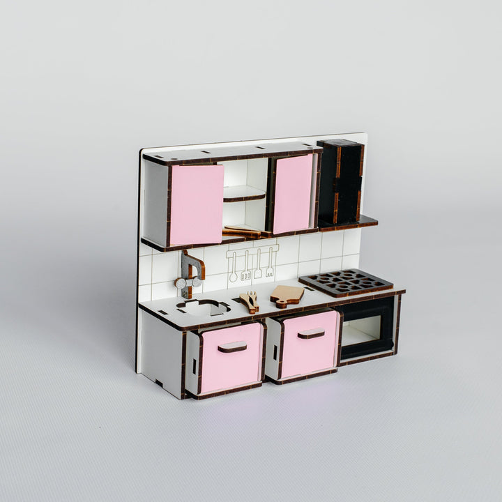 A miniature toy kitchen set with pink cabinets, a white tiled backsplash, and dark brown trim, shown on a neutral light gray background.