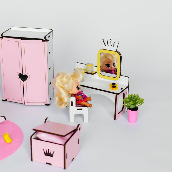 A miniature dollhouse furniture set featuring a pink wardrobe, vanity table with a yellow-framed mirror, a small pink chair, and a pink storage box, arranged on a light gray background.
