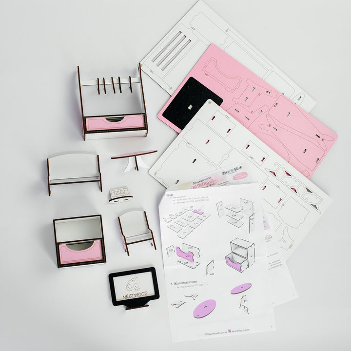 A miniature furniture assembly kit with various small wooden frames, pink drawer inserts, and instruction sheets laid out on a white surface.