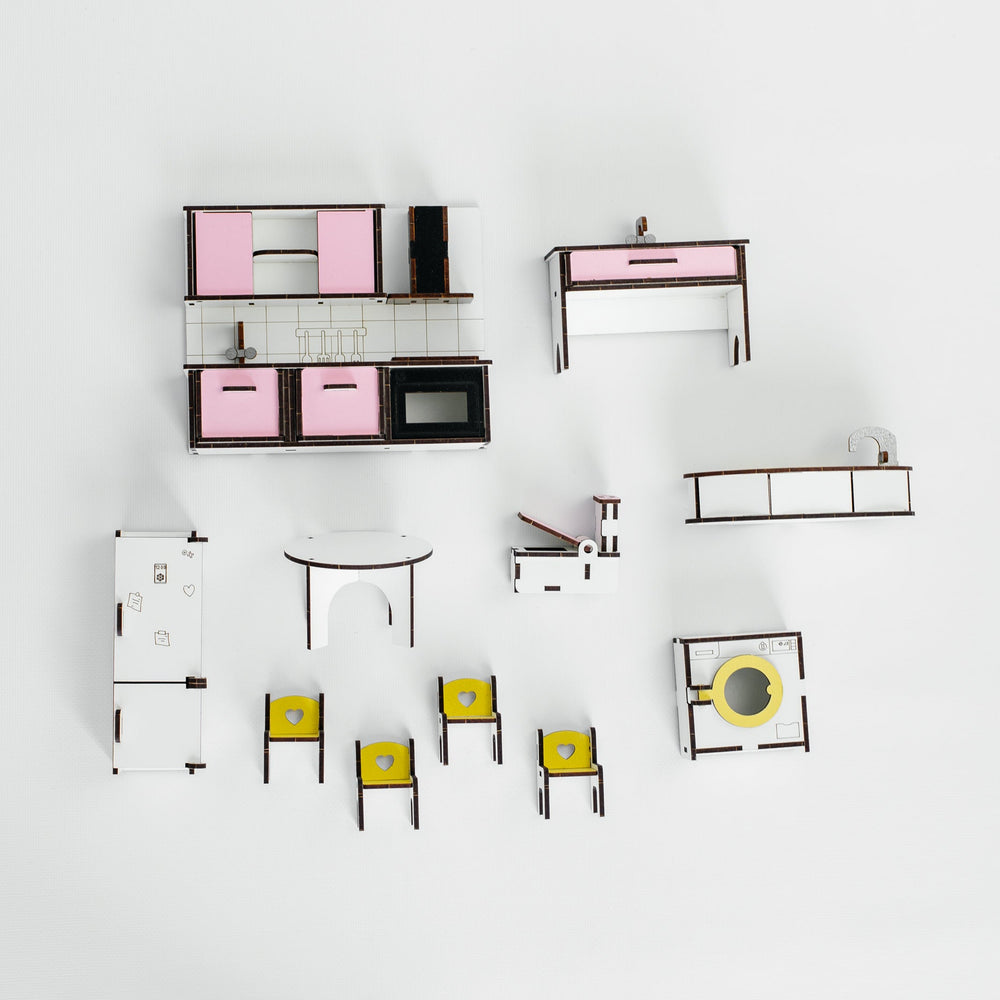 A top-down view of a miniature furniture set, including a kitchen island with pink cabinets, a desk, chairs, and other small furniture pieces, arranged on a clean white background.