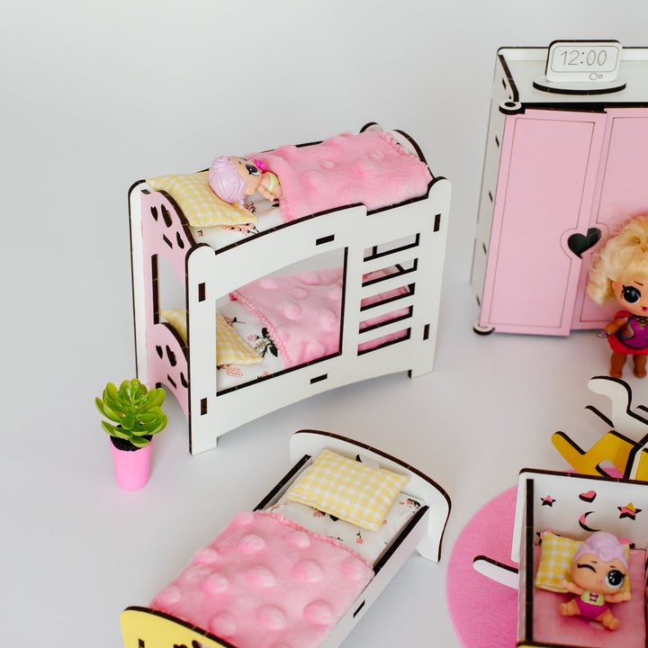 A miniature dollhouse bedroom set featuring a white wooden bed frame with pink bedding, a pink wardrobe, a small potted plant, and a yellow rocking horse, displayed on a white surface.