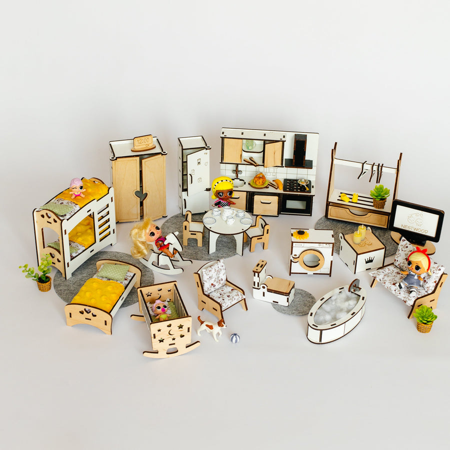 A miniature dollhouse furniture set arranged on a light gray surface against a white background. The set includes small beds, tables, chairs, cabinets, a kitchen, a washing machine, a computer desk, and tiny potted plants, with some pieces showing small doll figures.