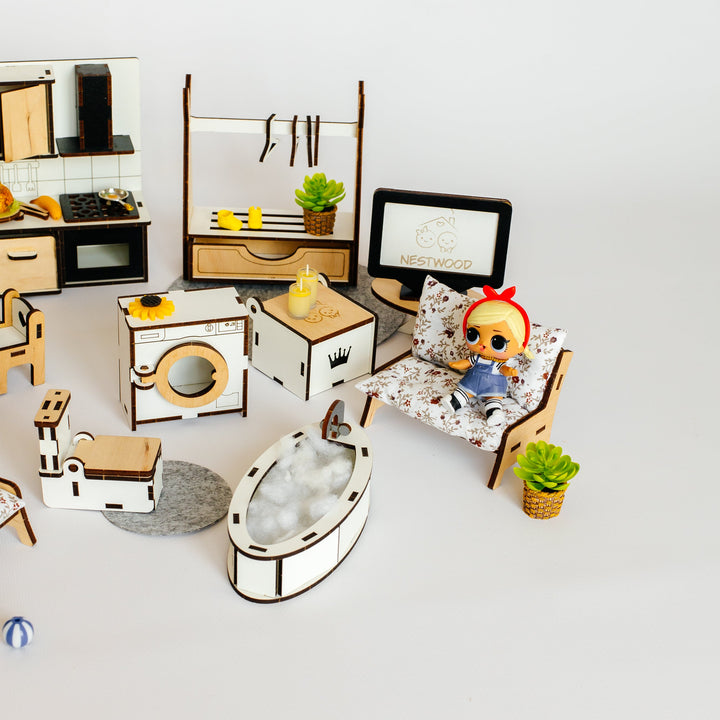 A miniature dollhouse furniture and room set displayed on a clean white background. The set includes a kitchen, bathroom, bedroom, and living room pieces in a small scale, with a small doll sitting in a chair.