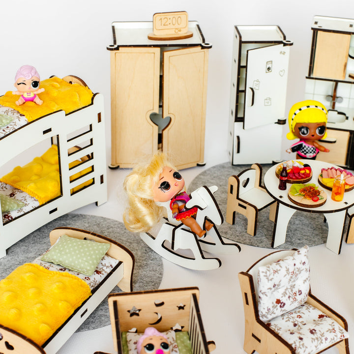 A dollhouse-style bedroom set with miniature furniture and small dolls, including beds, a wardrobe, refrigerator, table, chairs, rug, and accessories, arranged on a white surface against a white background.