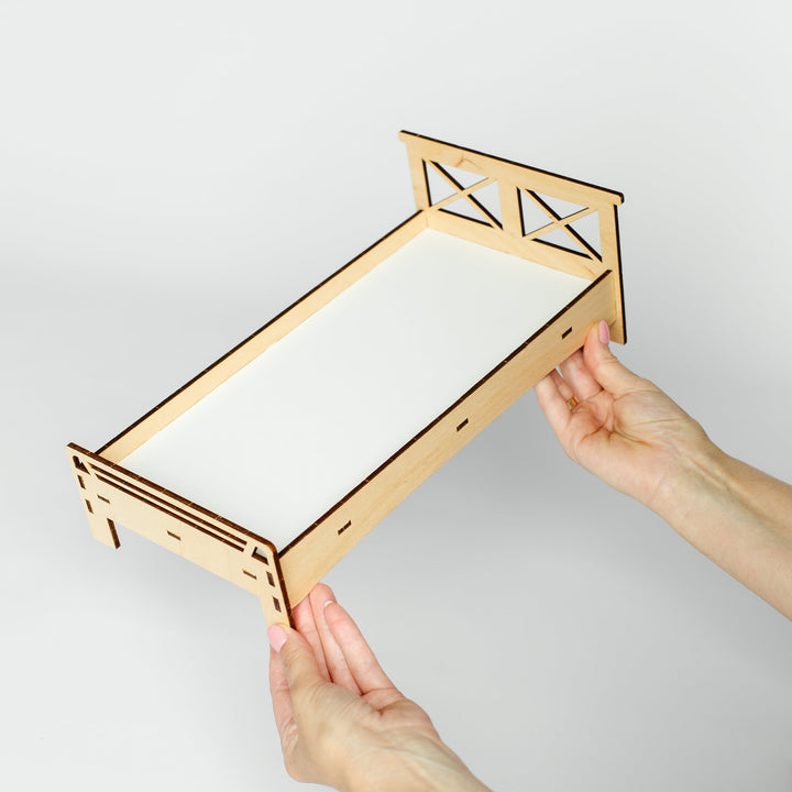 A person's hands holding a small, laser-cut wooden shelf or tray with a white insert, shown against a plain light gray background.