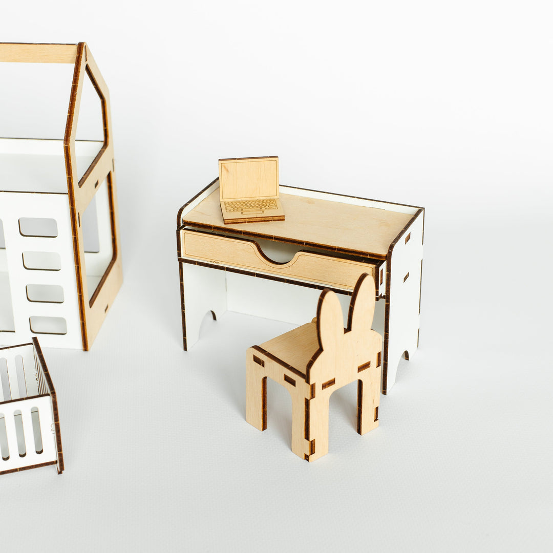 A minimalist wooden children's furniture set including a small desk with a drawer, a matching chair, and a small shelf, shown on a clean white background.