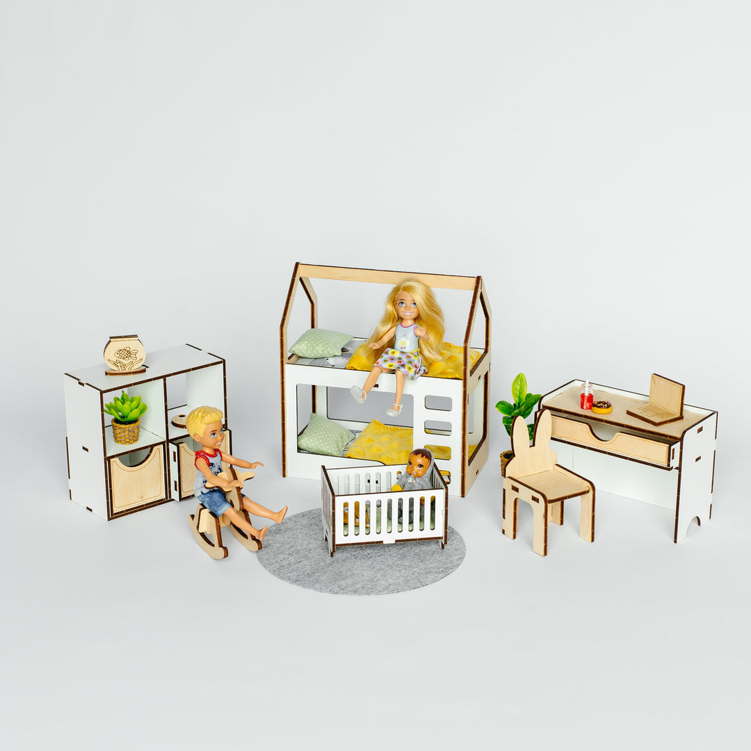 A miniature dollhouse-style nursery furniture set displayed on a light gray background. The set includes a house-shaped bed with a doll sitting inside, a crib, a desk with chair, and a cabinet with a small figurine, all crafted from light wood and white panels.