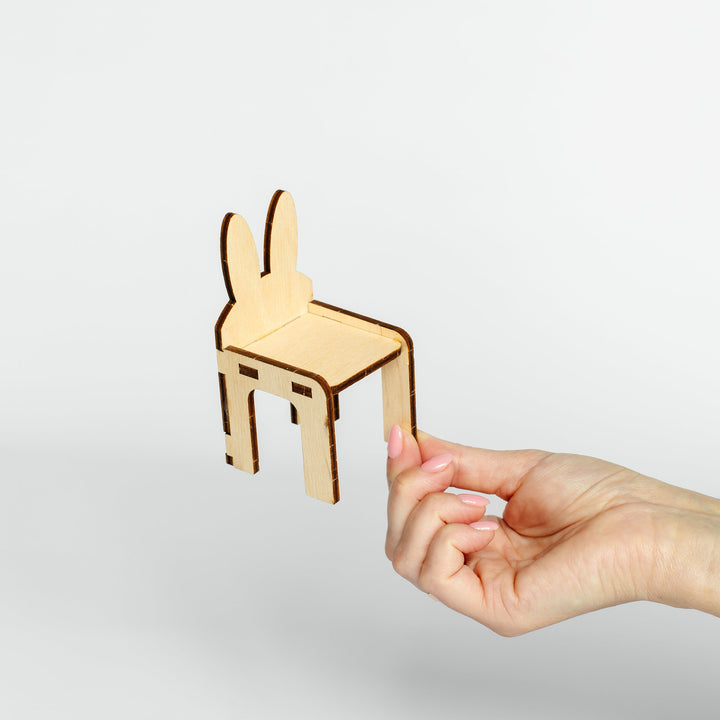 A small laser-cut wooden bunny-shaped chair held by a person's hand against a clean light gray background.