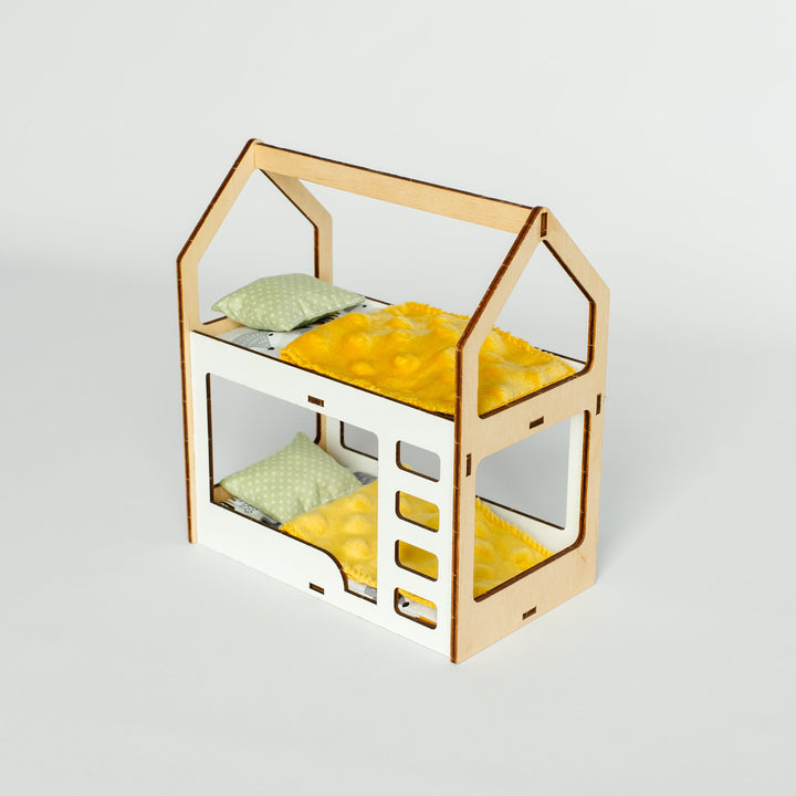 A miniature wooden house-shaped bed frame with a yellow patterned bedding set and two small pillows, shown on a light gray background.