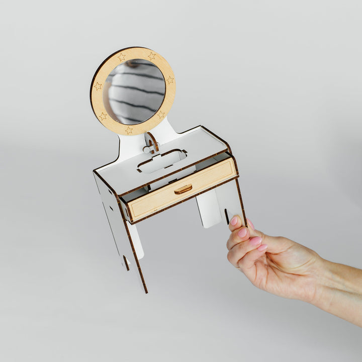A hand holding a small white and light wood vanity desk with an attached oval mirror, shown against a plain light gray background.