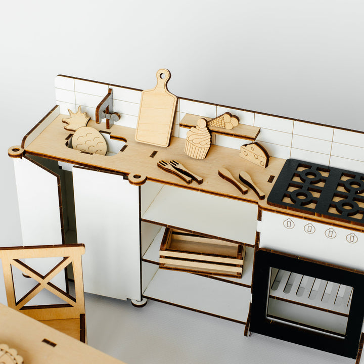 A miniature wooden toy kitchen set with a countertop, cabinets, stove, oven, sink, and various kitchen accessories, photographed against a plain light background.