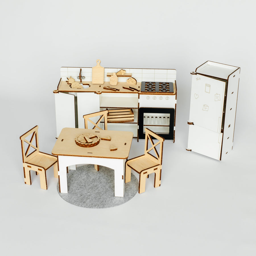 A miniature wooden dollhouse kitchen set featuring a dining table and two chairs, a small kitchen counter with stove and sink, and a tall refrigerator, all constructed from light-colored wood on a gray circular base against a white background.