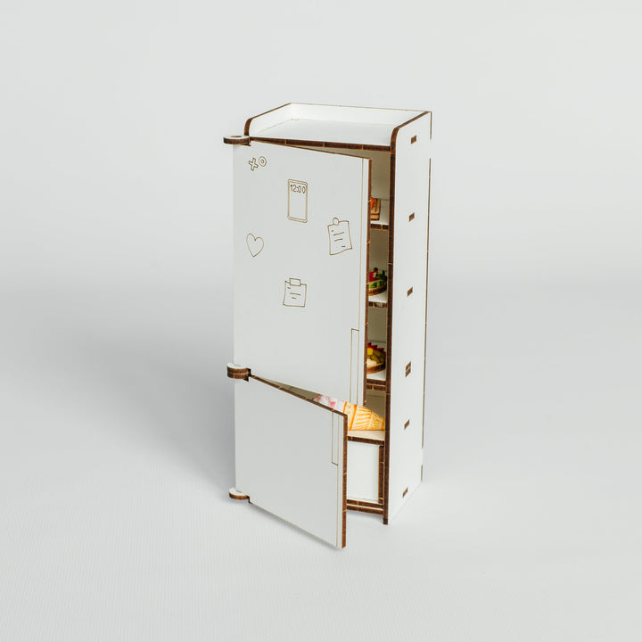 A miniature white toy refrigerator with an open door, showing a tiny interior with shelves and a small food container, set against a plain light gray background.