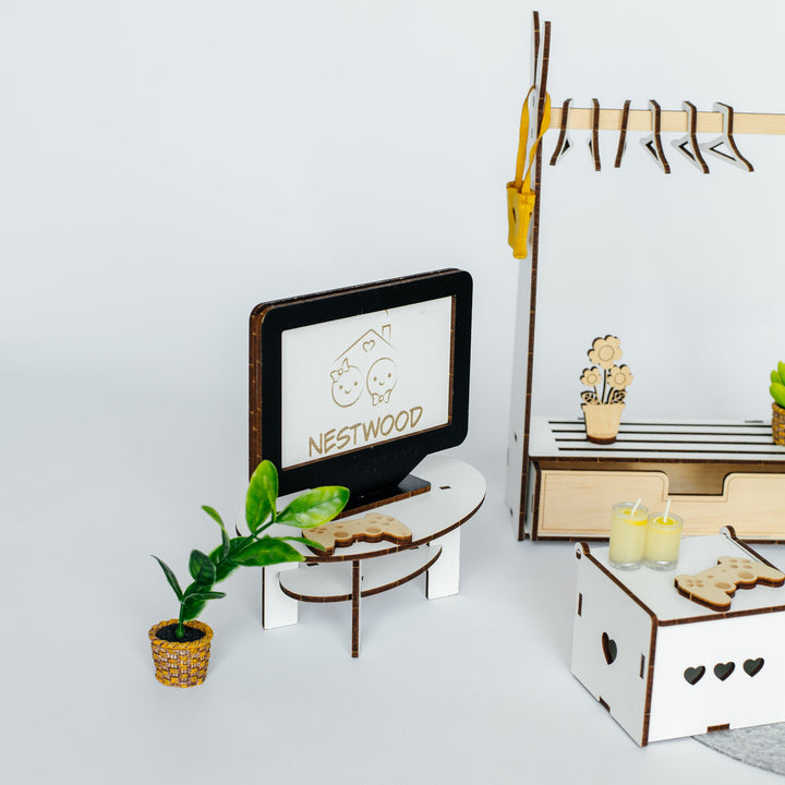 A miniature wooden toy furniture set featuring a small TV with 'NESTWOOD' branding, a potted plant, a small table, a hanging rack, and a storage box with heart-shaped cutouts, arranged on a light gray background.