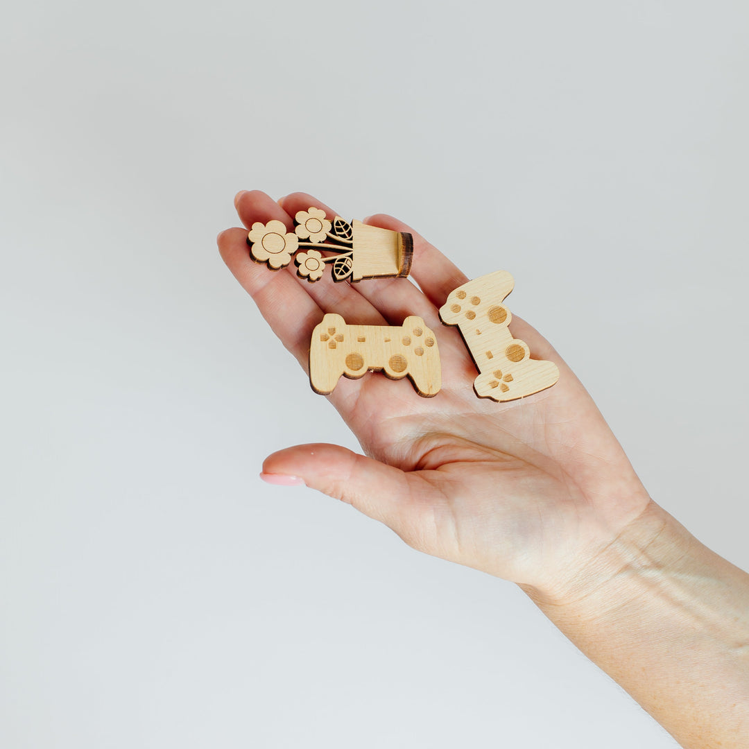 A hand holding three small wooden game controller-shaped accessories against a plain light gray background.