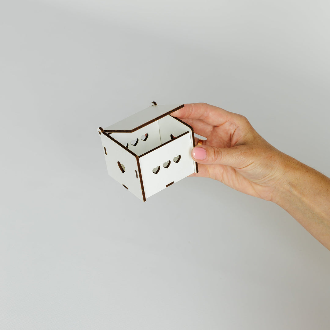 A hand holding a small white laser-cut cardboard box with brown edges against a plain light gray background.