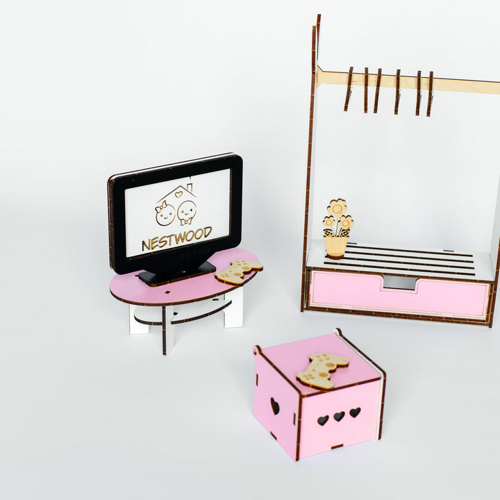A miniature pink and brown wooden toy furniture set, including a small TV stand with a TV displaying 'NESTWOOD', a clothing rack, and a pink storage box with heart cutouts, arranged on a white background.