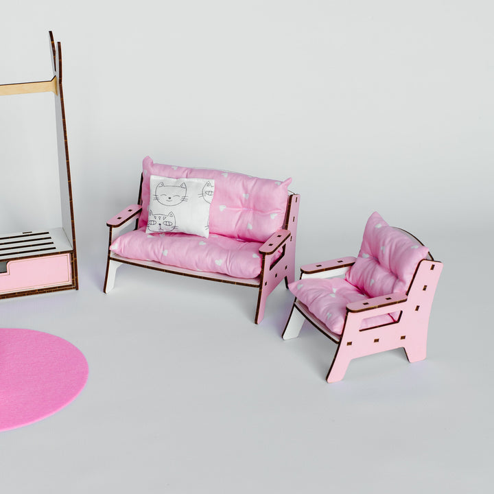 A miniature pink dollhouse furniture set featuring a two-seater sofa with a patterned cushion, a matching armchair, and a partial pink and wood cabinet on a light gray background.