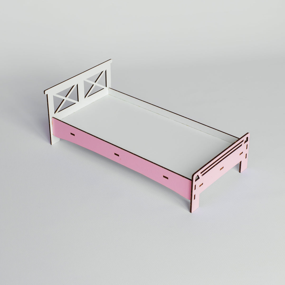 A small wooden bed frame with a pink footboard and white headboard, shown on a light gray studio background.