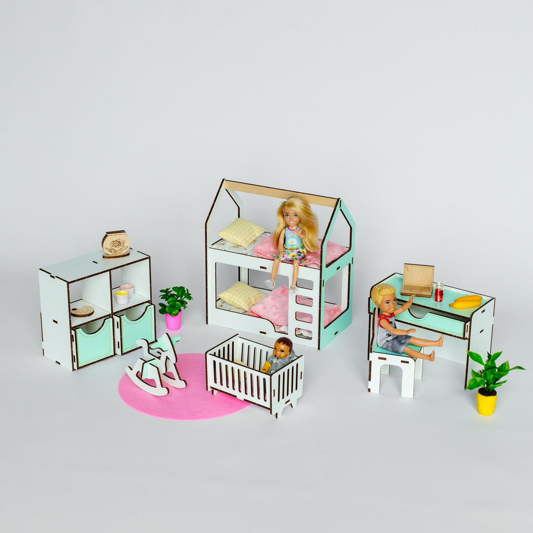 A dollhouse-style nursery furniture set displayed on a light gray studio background. The set includes a house-shaped bed with a doll inside, a crib, a small desk with chair, shelving, a pink rug, and miniature plants.