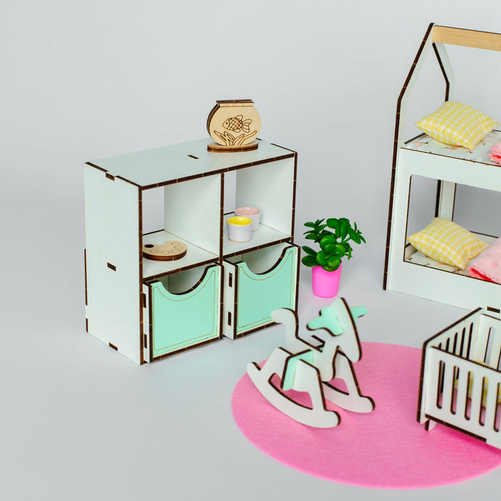 A miniature dollhouse playset featuring a white and mint green storage cabinet, a white rocking horse, a white crib, a pink rug, and a small potted plant, arranged on a light gray background.