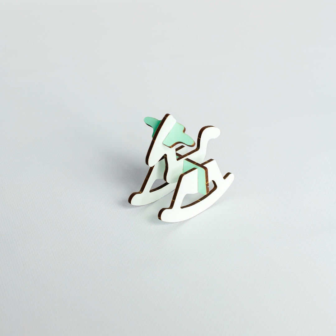 A small wooden rocking horse figurine with a mint green painted finish and natural brown wood edges, set against a plain light gray background.